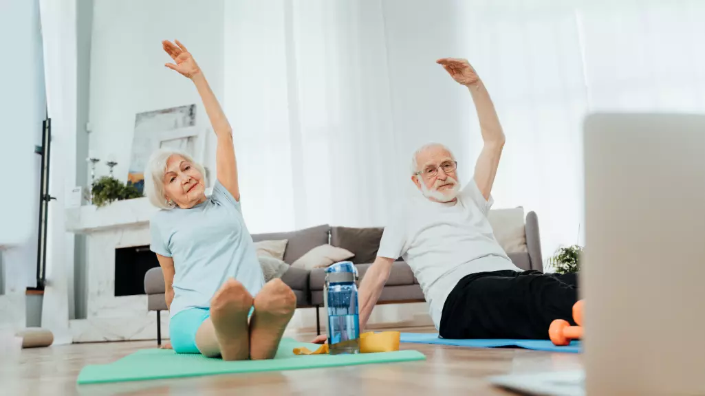 An elderly man and woman engaging in home fitness exercises."