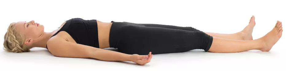 "Yoga practitioner in Savasana lying flat on back with arms at sides."
