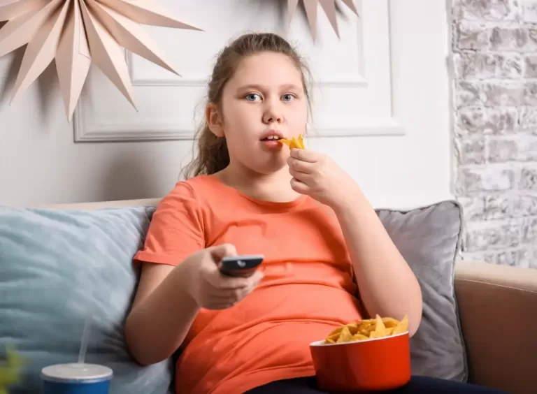 A photo of a girl sitting on a couch, eating unhealthy food."